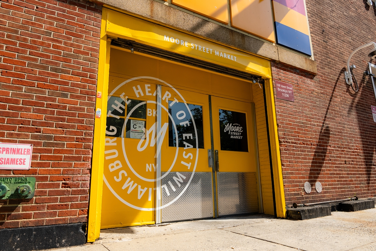 Exterior view of Moore Street Market building with colorful yellow door and logo.